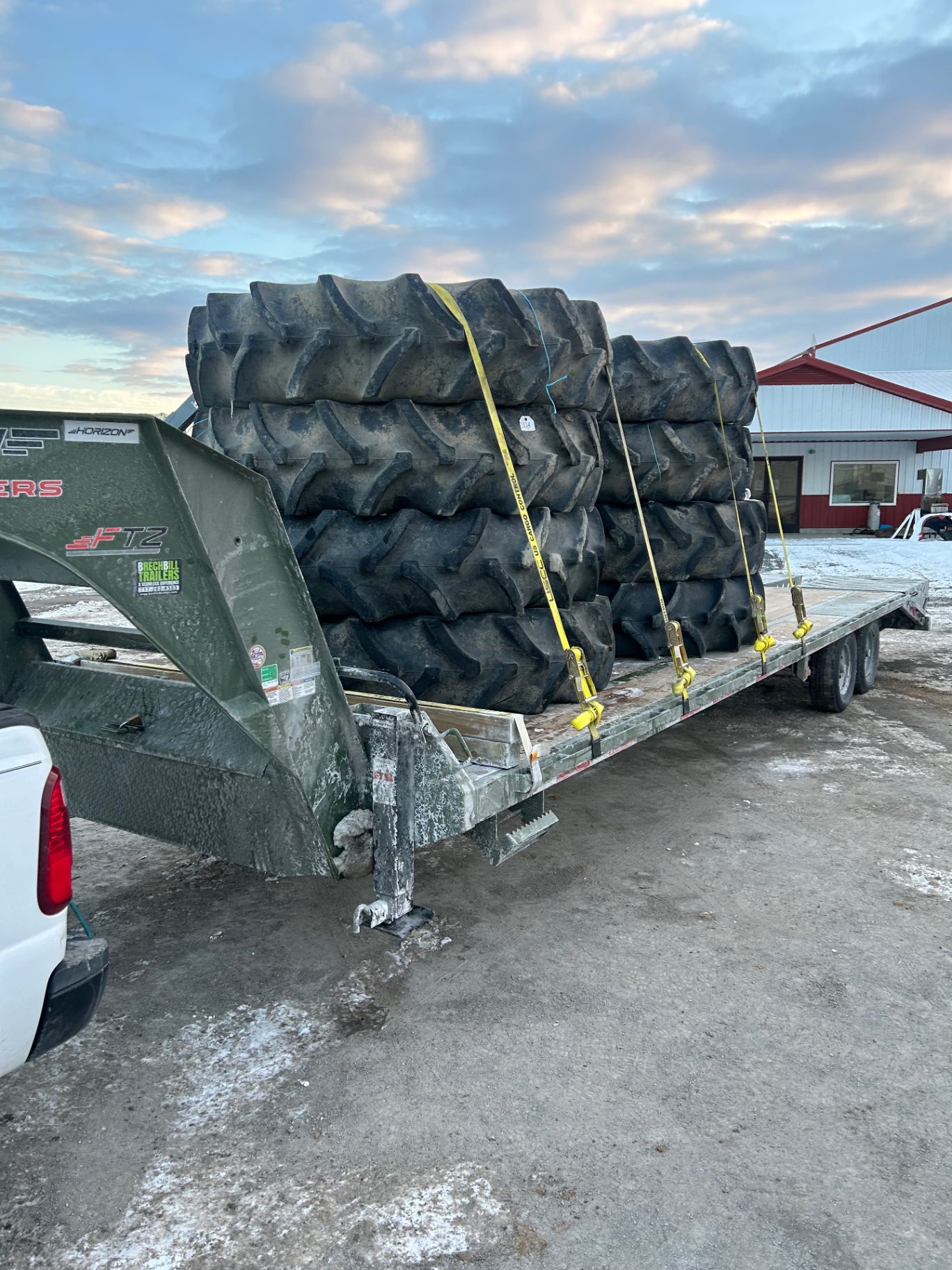 Stacked agricultural tractor tires strapped on a gooseneck trailer