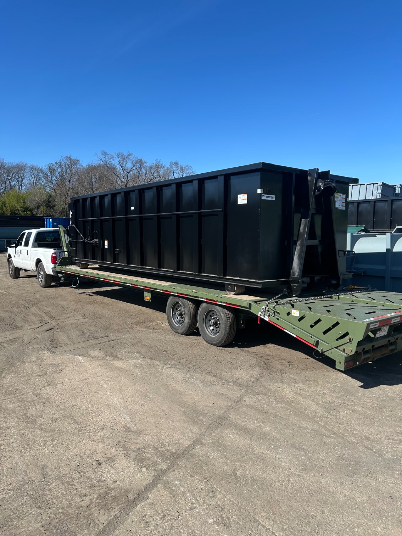 Roll-off dumpster container loaded on a BigWay gooseneck trailer